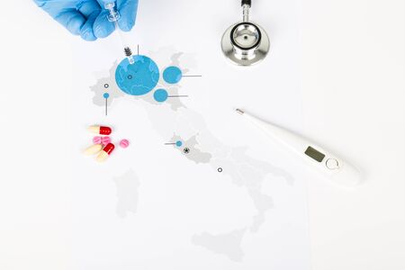 Novel Covid-19, Italy map paper with blue areas infected, on white background. Copy space. with human hand with blue gloves and thermometer, pills, syringe, stethoscopeの写真素材