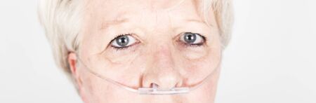 Mature caucasian european woman with blond hair and anxious behaviour, wearing an oxygene tube in nose to breathe because infected by coronavirus. Covid-19 in Europe, Franceの写真素材