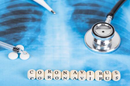 Text phrase Coronavirus with wooden letter on lungs radiology blue image background, with stethoscope, pills, tablets, syringue vaccine and thermometerの写真素材