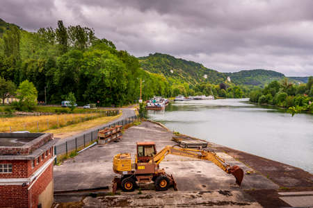 Illustrative Editorial Poclain brand. Large view by wide angle on Seine River in France, with excavator on the dock. Canal boats on the river, parked. Vibrant colors, good lights, cloudy skyのeditorial素材