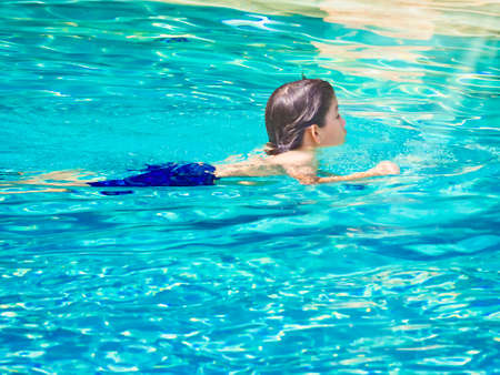 Cheerful teenager boy swimming in crystal turquoise water at summer time with good sun light