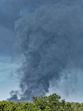 A Burning plastic recycling place causes a big pile of dark, black thick smoke on a sky blue summer...