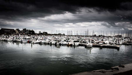 SAINT VAAST, FRANCE - SEPTEMBER Circa, 2020. Dramatic cloudy Sky landscape on the harbor with sailboats. Panorama, dark pessimist atmosphere feelings. Desaturated imageのeditorial素材