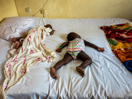 MBOUR, SENEGAL - DECEMBER Circa, 2020. Two African little infant and baby wearing diaper and sleeping on bed with comfort. On dirthy white bed, poverty in Africaのeditorial素材