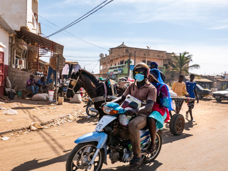 MBOUR, SENEGAL - DECEMBER Circa, 2021. Few women and men with   Virus mask walking, driving in...