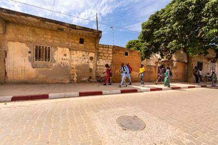 MBOUR, SENEGAL - JANUARY Circa, 2021. Unidentified school aged girls and boys with backpack walking in the poor village after school in sunny spring day. No face mask during Covid 19 pandemy.のeditorial素材
