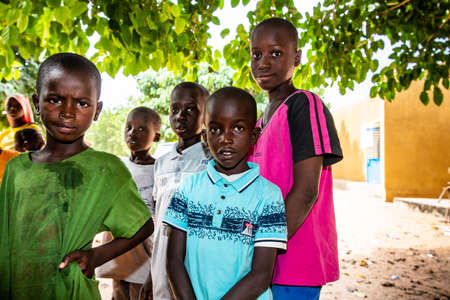 MBOUR, SENEGAL - DECEMBER Circa, 2020. Group of unidentified teenagers standing up in playground of the school, outdoors on a sunny summer day. Waiting for new bags given by international ngo. Sad and poor children.のeditorial素材