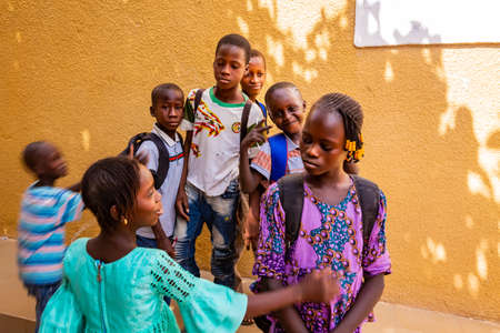 MBOUR, SENEGAL - DECEMBER Circa, 2020. Group of unidentified teenagers standing up in playground of the school, outdoors on a sunny summer day. Waiting for new bags given by international ngo. Poor rural children.のeditorial素材