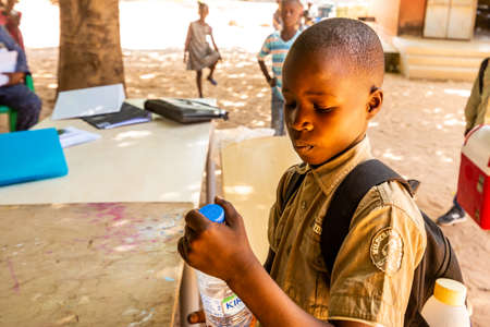 MBOUR, SENEGAL - DECEMBER Circa, 2020. Group of unidentified teenagers standing up in playground of the school, outdoors on a sunny summer day. Happy to get new bags given by international ngo. Poor rural children.のeditorial素材