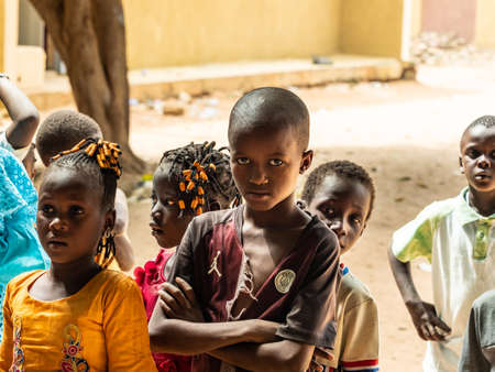 MBOUR, SENEGAL - DECEMBER Circa, 2020. Group of unidentified teenagers standing up in playground of the school, outdoors on a sunny summer day. Waiting for new bags given by international ngo. Poor rural children.のeditorial素材