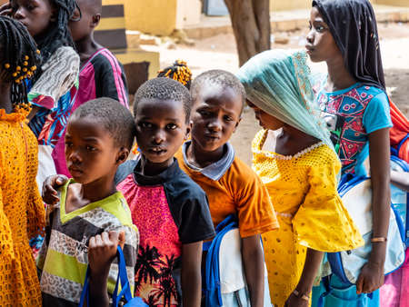 MBOUR, SENEGAL - DECEMBER Circa, 2020. Group of unidentified teenagers standing up in playground of the school, outdoors on a sunny summer day. Waiting for new bags given by international ngo. Poor rural children.のeditorial素材