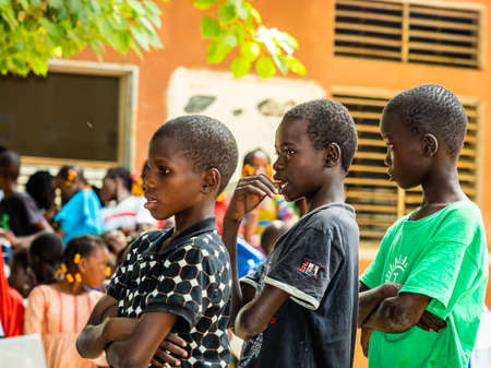 MBOUR, SENEGAL - DECEMBER Circa, 2020. Group of unidentified teenagers standing up in playground of the school, outdoors on a sunny summer day. Waiting for new bags given by international ngo. Poor rural children.のeditorial素材