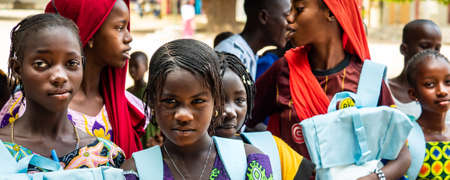 MBOUR, SENEGAL - DECEMBER Circa, 2020. Group of unidentified teenagers standing up in playground of the school, outdoors on a sunny summer day. Happy to get new bags given by international ngo. Poor rural children.のeditorial素材