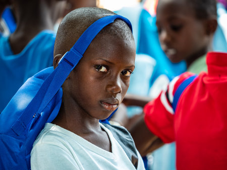 MBOUR, SENEGAL - DECEMBER Circa, 2020. Unidentified sad poor teenager standing in playground of the school, outdoors on a sunny summer day. With school bag on head. African povertyのeditorial素材
