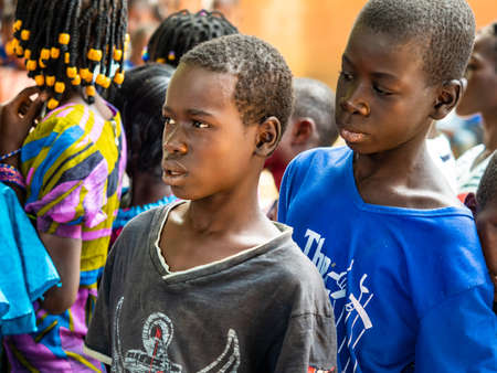 MBOUR, SENEGAL - DECEMBER Circa, 2020. Group of unidentified teenagers standing up in playground of the school, outdoors on a sunny summer day. Waiting for new bags given by international ngo. Poor rural children.のeditorial素材