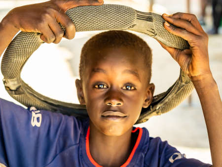 MBOUR, SENEGAL - JANUARY Circa, 2021. Portrait of unidentified young senegalese child with rubber wheel on head, looking at camera. Happy feeling and poverty. outdoorsのeditorial素材