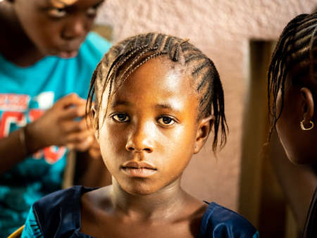 MBOUR, SENEGAL - JANUARY Circa, 2021. Unidentified child girl with sad anxious face, thinking about way of life in poor african village.のeditorial素材