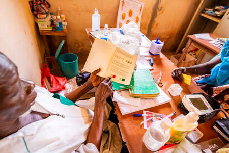 MBOUR, SENEGAL - Circa DECEMBER 2021. Unidentified elderly black doctor during consultation in dispensary health care center in village in small rudimentary local with cheap equipment. Poverty in Africaのeditorial素材