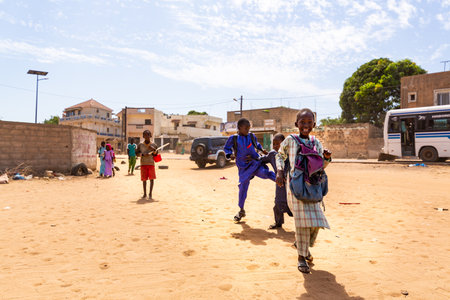MBOUR, SENEGAL - JANUARY Circa, 2021. Unidentified school aged boys with backpack walking in the poor village, fighting, smiling, after school in sunny spring day. No face mask during Covid 19 pandemic.のeditorial素材