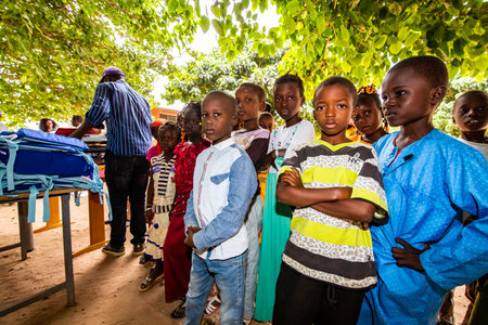 MBOUR, SENEGAL - DECEMBER Circa, 2020. Group of unidentified teenagers standing up in playground of the school, outdoors on a sunny summer day. Waiting for new bags given by international ngo. Sad and poor children.のeditorial素材