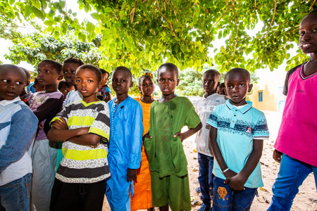 MBOUR, SENEGAL - DECEMBER Circa, 2020. Group of unidentified teenagers standing up in playground of the school, outdoors on a sunny summer day. Waiting for new bags given by international ngo. Sad and poor children.のeditorial素材