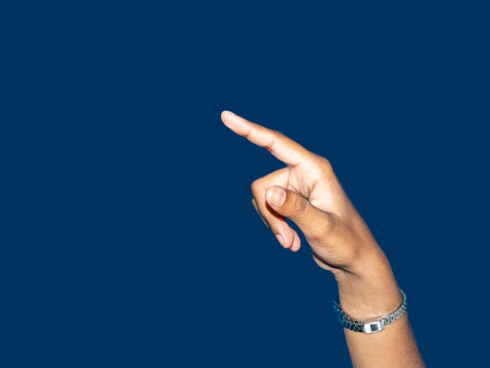 Close up of a young indian woman hand pointing finger as touching screen, isolated on blue...