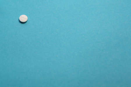 Isolated white medical pill to cure illness for sick patient given by doctor at hospital on blue background with place for textの写真素材