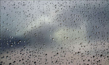Water drops on the window with a cloudy sky background. Drops of rain on the window.