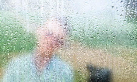 Water drops on glass with blurred man in the background. Rainy day.の写真素材