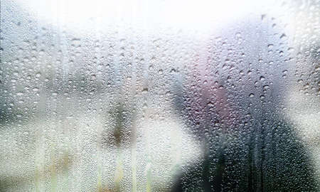 Rain drops on the window, close-up. Blurred silhouette of a man in the background.