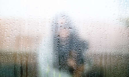 Close-up view of a woman behind the glass with raindrops