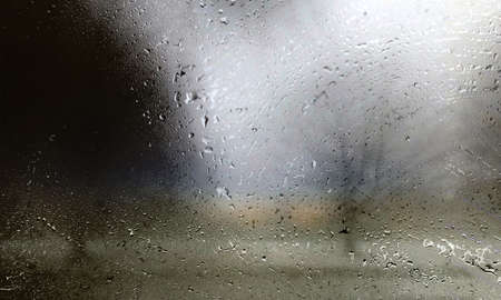Drops of rain on the window with a blurred silhouette of a person.