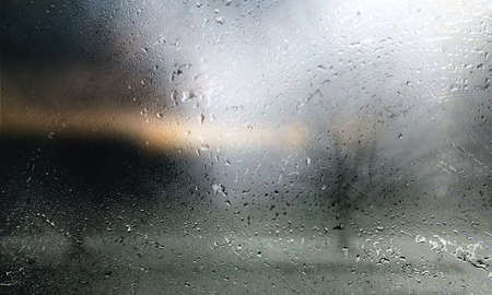 Rain drops on a window glass with a silhouette of a man in the background