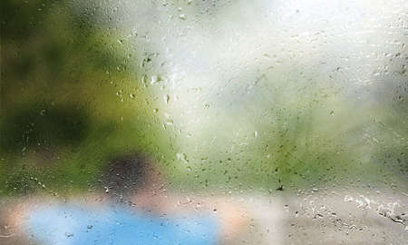 Rain drops on window glass with blurred background of man in park.