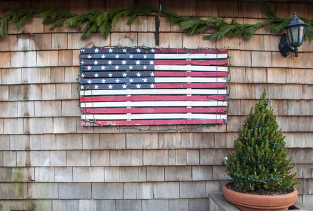 A vintage wooden flag attached to the side of a building with a small potted pine tree covered in holiday lightsの写真素材