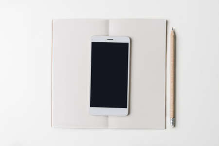 Top view of office workplace. White desk with copy space. Flat lay view on table with opened notebook, pen and phone. Creative designer concept.の写真素材