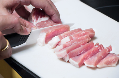 Woman cutting raw pork on white plate, prepare for cookingの写真素材