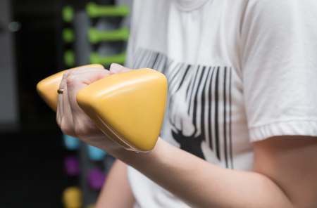 Woman working out at home with holding yellow barbell dumbbell at fitness gymの写真素材