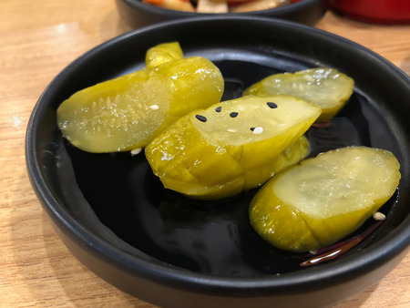 Black bowl of chopped pickled cucumber sprinkled with some black and white sesameの写真素材
