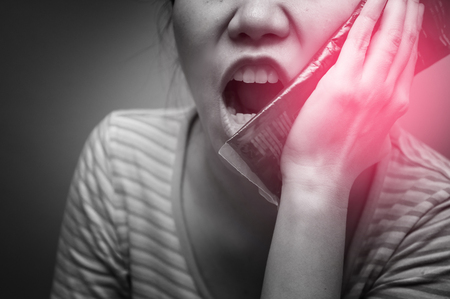 Asian woman suffering from toothache and using cold pack jelly on red spot. Concept of teeth problem.の写真素材
