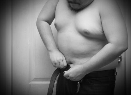 Overweight man trying to fasten too small jean pants.Black and white tone, Represent of fat, obesity, big belly.の写真素材