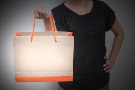 Close-up of female customer holding paper shopping bag on grayの写真素材