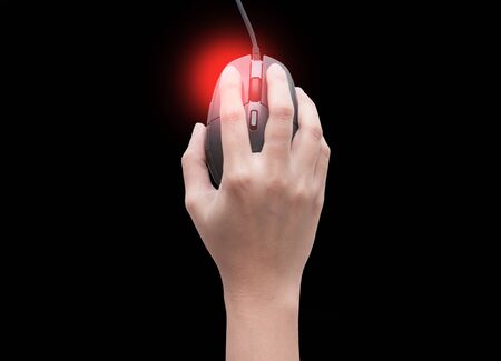 Top view of female hands clicking computer mouse isolated on black background with red spot on her finger. finger pain. Arthritis disorderの写真素材