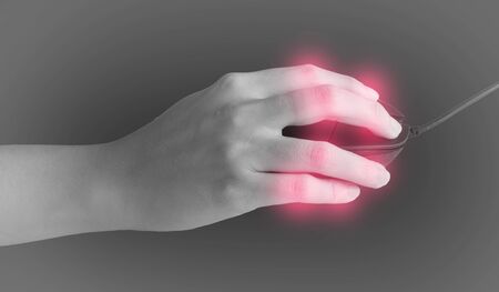 female hands clicking computer mouse isolated on black background with red spot on her finger. finger pain. Arthritis disorderの写真素材
