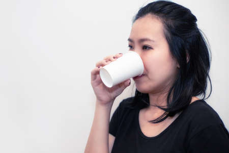 Asian young woman drinking a fresh white paper cup of water or other beverage. Black and white toneの写真素材