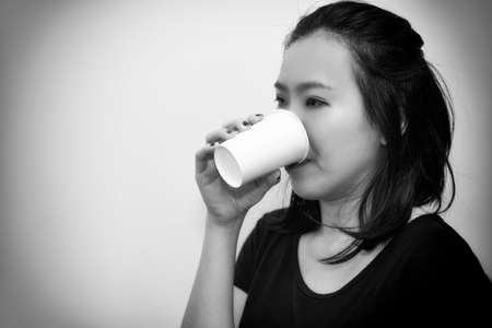 Asian young woman drinking a fresh white paper cup of water or other beverage. Black and white toneの写真素材