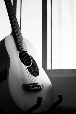 Acoustic guitar resting on guitar stand hanger with black and white toneの写真素材