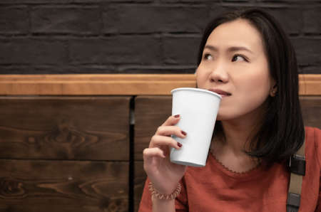 Asian young woman drinking a fresh white paper cup of water or other beverage.の写真素材