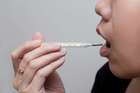 Asian woman measuring oral temperature by medical thermometer or clinical thermometer. Covid-19...