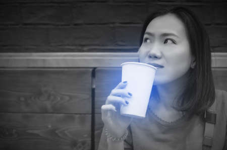 Asian young woman drinking a fresh white paper cup of water or other beverage. Black and white tone.の写真素材